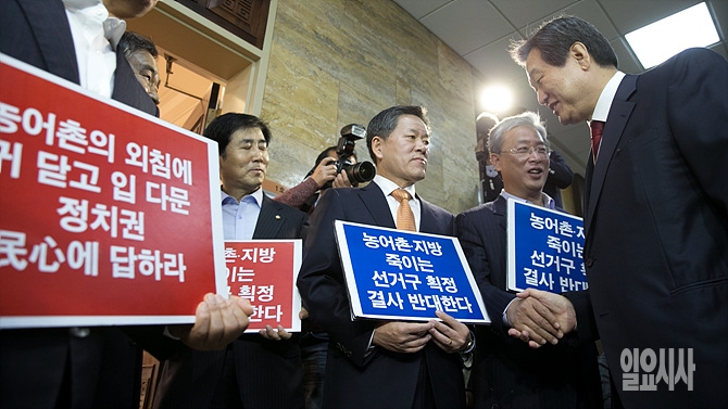지난달 12일, 서울 여의도 국회서 선거구획정 문제 등을 논의하기 위한 '여야4+4회동'에 앞서 새누리당 김무성 대표(사진 오른쪽)이 웃으며 획정을 반대하며 피켓을 들고 있는 새정치민주연합 주승용(사진 가운데)·유성엽 의원 등 농어촌 소속 의원들을 바라보며 웃고 있다.